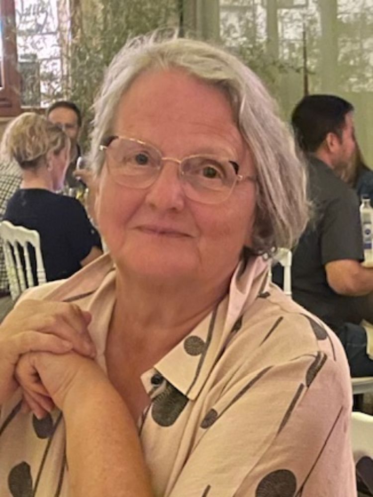 Anne Copley sitting down at dinner smiling at the camera, wearing glasses and a spotty top